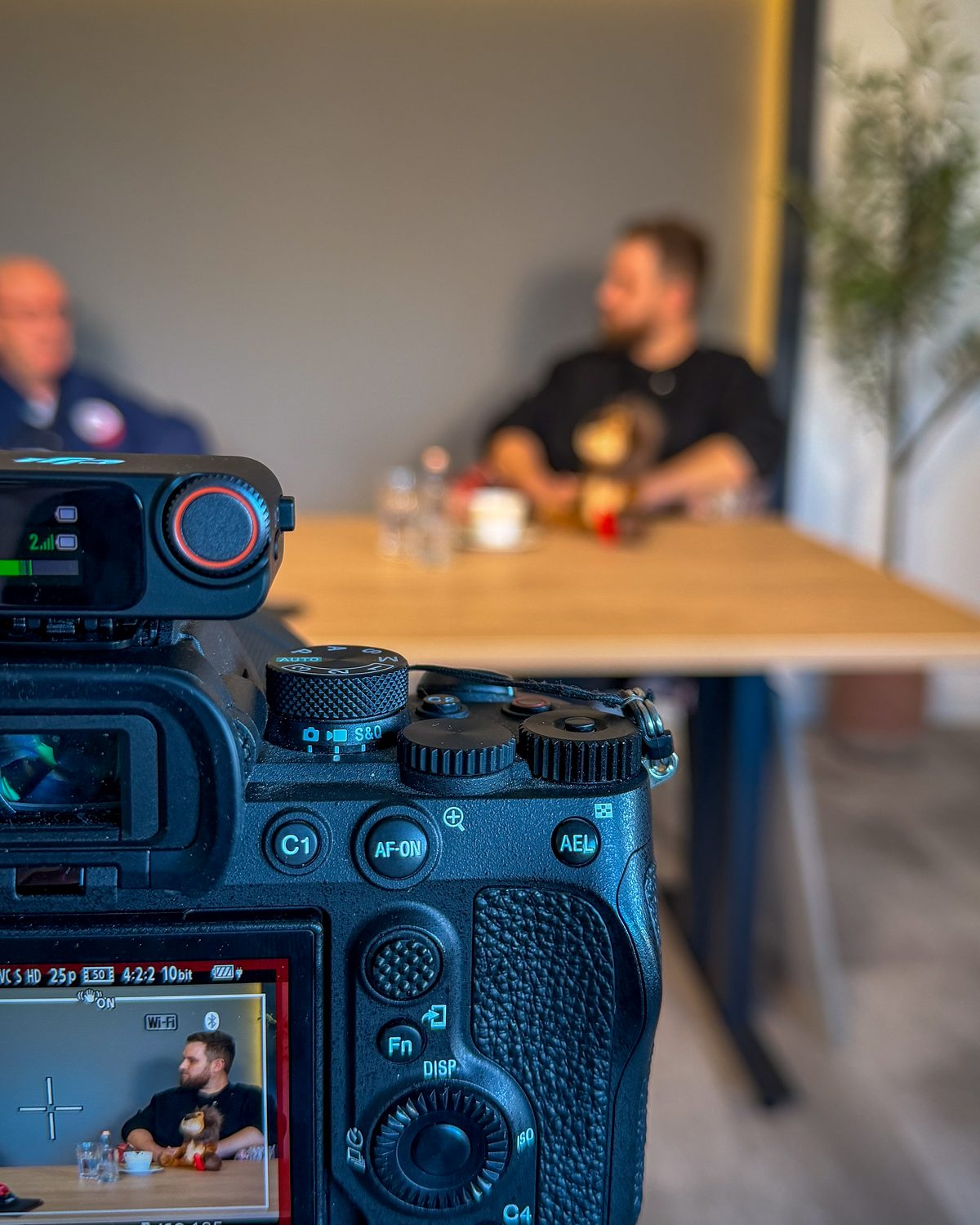 Kamera im Vordergrund beim Interviewdreh in einem Bremer Kfz-Betrieb, Gesprächspartner am Tisch