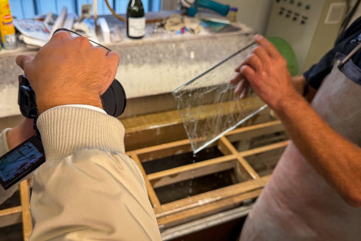 Eine Glasscheibe wird aus dem Wasserbad gehoben, der Kameramann filmt die Szene in der Glaserei Wolff