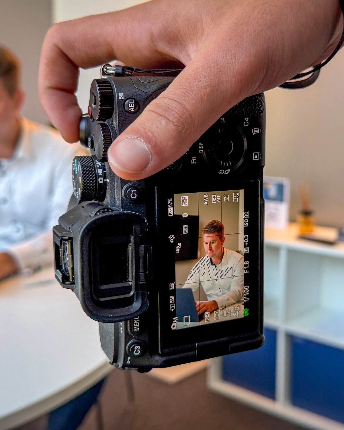 Kameradisplay zeigt einen Unternehmer am Laptop, Porträtaufnahme für LinkedIn im Büro