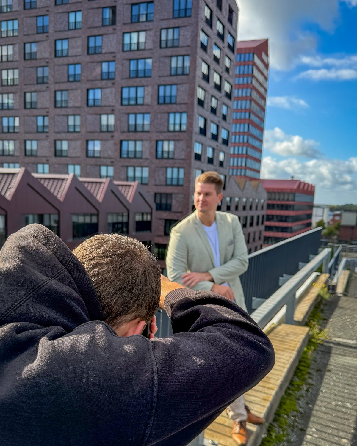 Fotograf fotografiert einen Unternehmer im hellen Sakko vor Backsteinhochhäusern