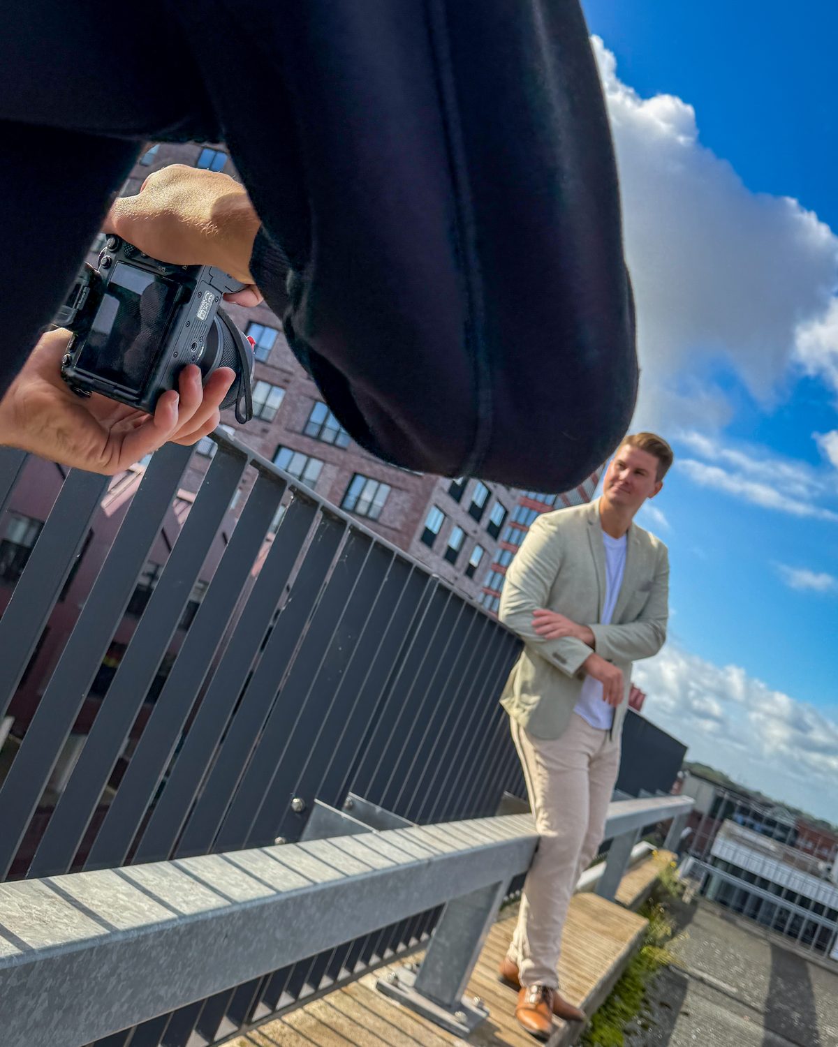 Fotoshooting aus der Froschperspektive: Unternehmer lehnt am Geländer einer Dachterrasse, links die Kamera