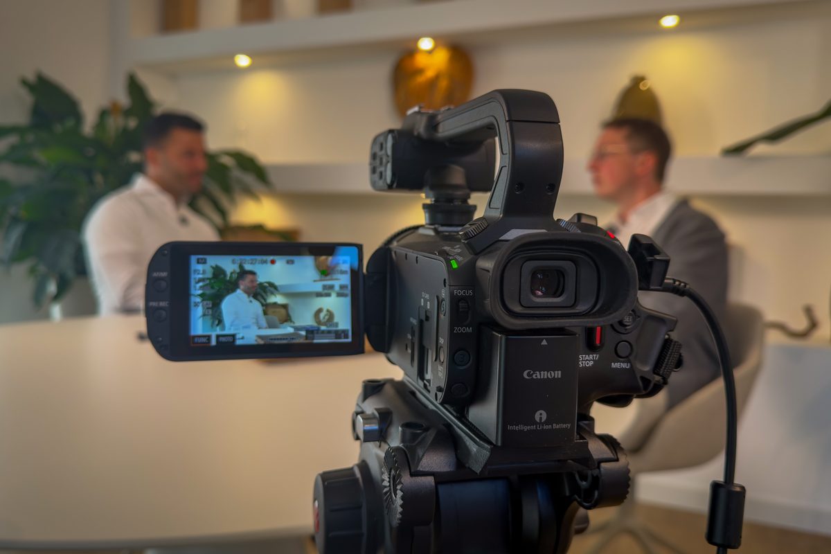 Podcast-Aufzeichnung in einem Büro: Camcorder im Vordergrund, zwei Gesprächspartner am Tisch