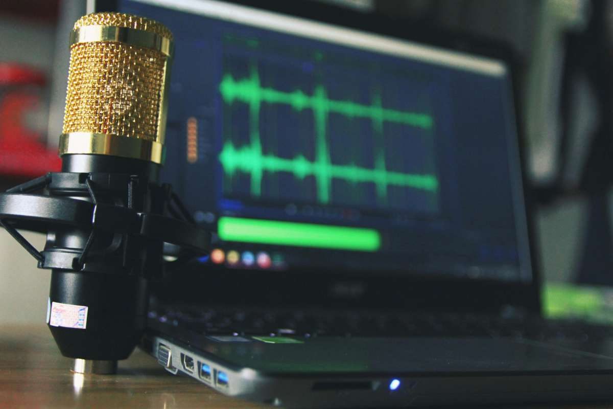 Podcast-Mikrofon vor einem Laptop mit Audiospur auf dem Bildschirm