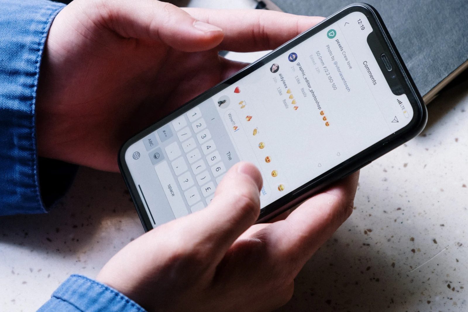 Hände halten ein Smartphone, auf dem eine Chat-Nachricht mit Emojis geschrieben wird
