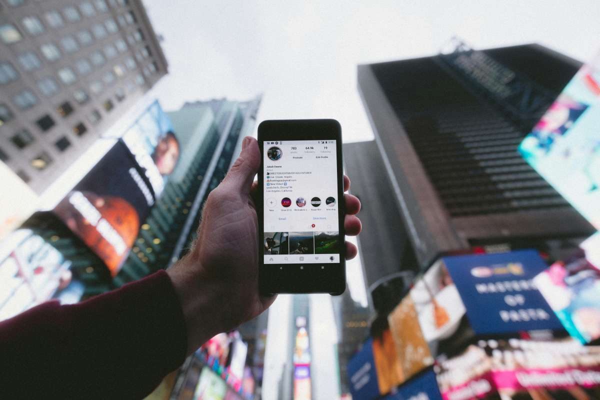 Hand hält ein Smartphone mit Instagram, umgeben von einer Collage aus Social-Media-Bildern